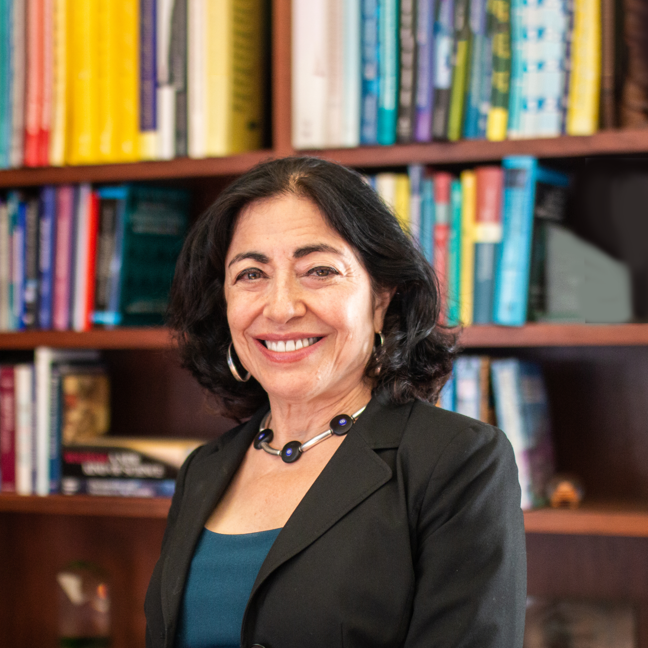 Dean Jennifer Chayes smiling facing the camera, standing against a bright multicolor bookshelf 