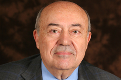 Portrait of Andrew Viterbi wearing grey suit against a brown backdrop