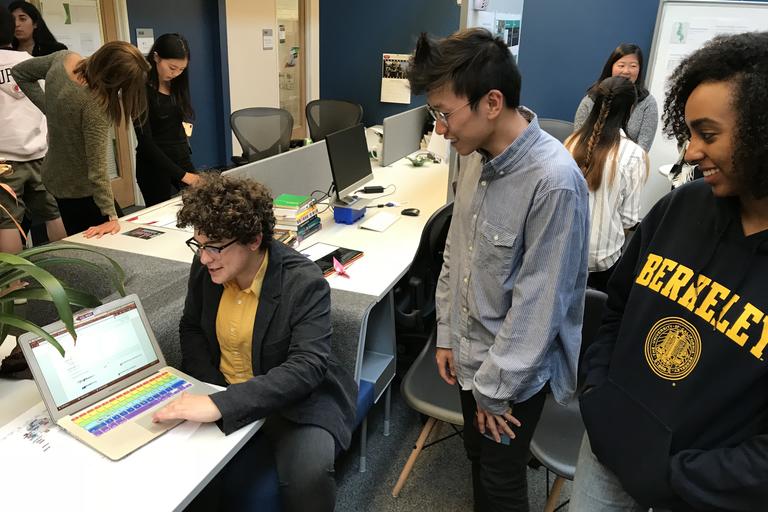 two students looking over the shoulder of a third student at a computer screen with graphs displayed on it