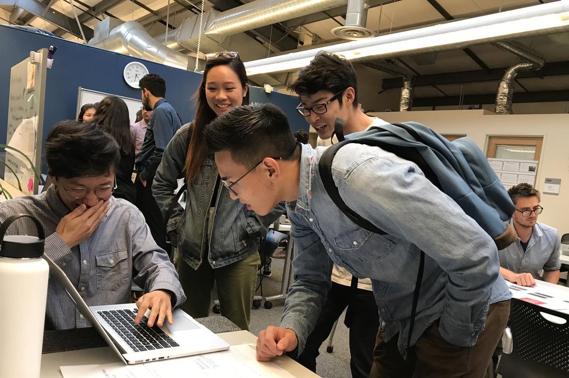 Four students gathering around a laptop, laughing, at the Spring 2018 semester Data Scholars project showcase.